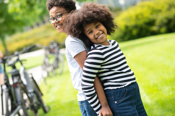 Two friends boy and girl having fun in park standing back to back playing outdoor during summer vacation. - Foto, Imagen