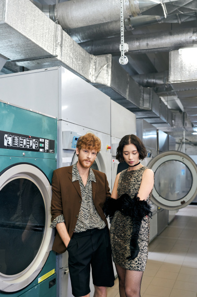 giovane coppia multietnica alla moda in piedi vicino alle lavatrici nella lavanderia pubblica - Foto, immagini