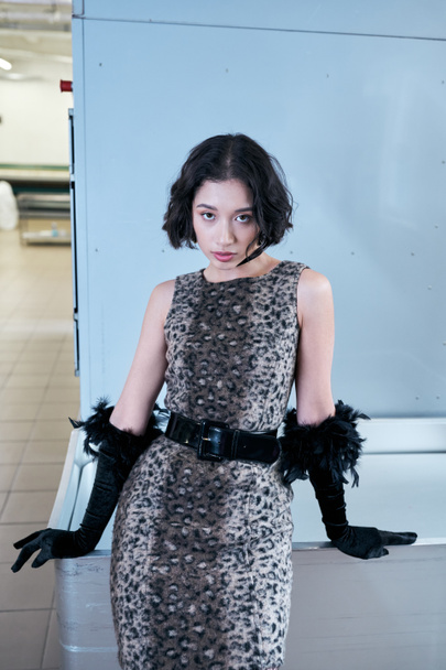 mladá asijská žena v šatech a rukavice při pohledu na kameru při pózování ve veřejném prádle - Fotografie, Obrázek