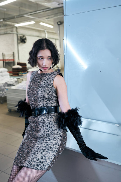 trendy young asian woman in dress with animal print and gloves standing in public laundry - Zdjęcie, obraz