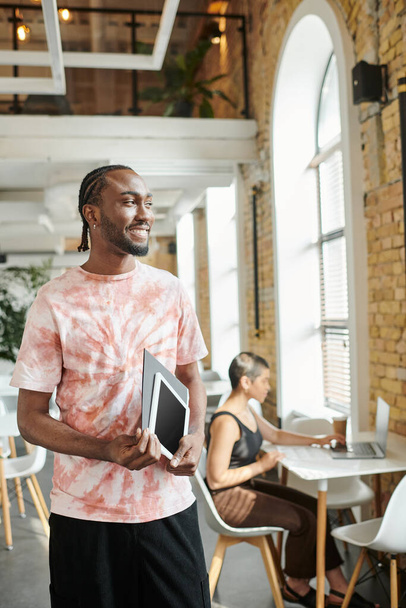allegro uomo africano americano in possesso di tablet, cartella, guardando lontano vicino a collega di lavoro femminile, start-up - Foto, immagini