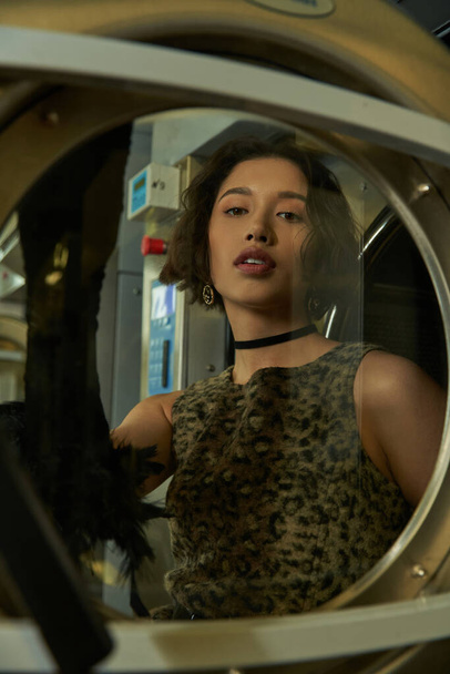 fashionable young asian woman standing behind glass of washing machine in coin laundry - Photo, Image