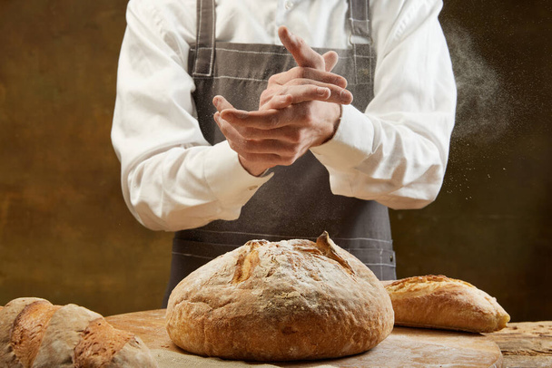 Baker cocinando pan. El hombre abofetea harina sobre la masa. Manos de hombre con aplauso de harina. Concepto de comida, cocina, tradiciones, panadería y publicidad - Foto, imagen