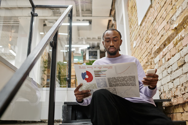 homme d'affaires, homme afro-américain tenant des graphiques et smartphone, assis sur les escaliers, coworking, startup - Photo, image