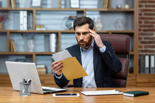 Upset and angry boss received mail message notification with bad news, male businessman working inside office with documents and papers, using laptop at work. - Zdjęcie, obraz