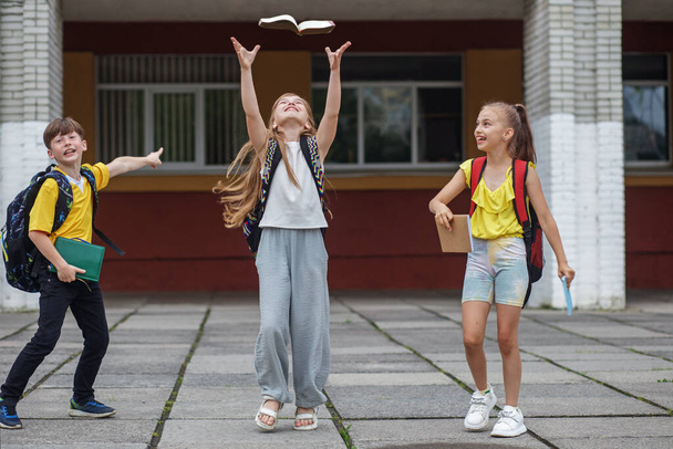 Vissza a suliba. Iskolai leckék kezdete. Három iskolás gyerek szórakozik a szabadban. Hátizsákkal rendelkező osztálytársak. - Fotó, kép