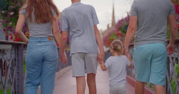 Θετικοί γονείς και παιδιά περπατώντας γέφυρα με πολύχρωμα λουλούδια. Η ευτυχισμένη οικογένεια περνάει χρόνο έξω. Χαρούμενο ζευγάρι με παιδιά περπατά στο πάρκο. Χαμογελαστή οικογένεια διασκεδάζει έξω. - Πλάνα, βίντεο