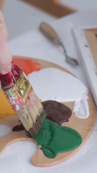 The hand of a young artist mixes paints on a palette that stands on the table. Basic colors. Work with a thick paintbrush. Workplace of the artist - Video