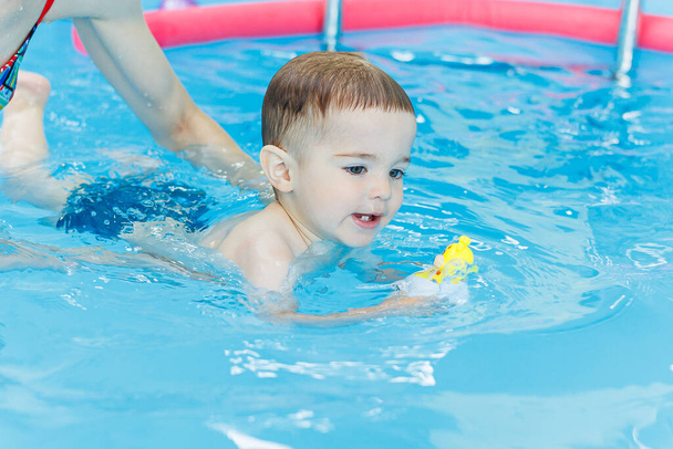 2歳の少年がプールで泳ぐことを学んでいる. 子供のための水泳のレッスン. 子供のための水泳学校. - 写真・画像