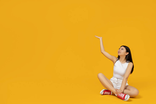 Chica asiática señalando su mano a la montaña, sobre un fondo amarillo, con espacio para el texto - Foto, Imagen