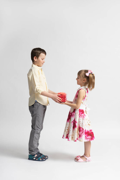De jongen wenst een gelukkige verjaardag en geeft het jongere meisje een kerstcadeau. broer en zus poseren op een witte achtergrond. - Foto, afbeelding