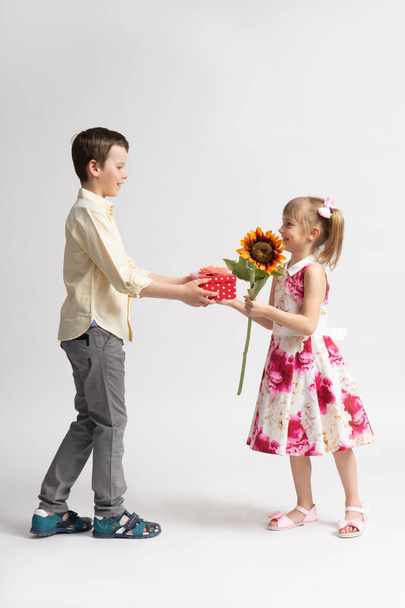 Хлопчик бажає щасливого дня народження і дарує молодшій дівчині святковий подарунок. Брат і сестра позує на білому тлі. - Фото, зображення