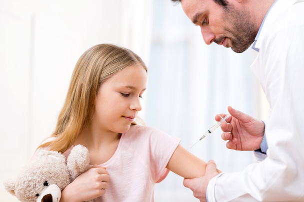 Молоду маленьку дівчинку вакцинують у лікаря
 - Фото, зображення