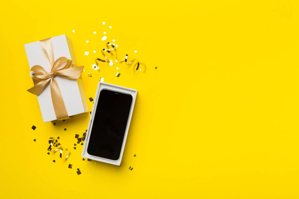 Opened gift box with gold ribbon and smartphone on color background, top view. Blank open box packaging mockup , Template for your design - branding mockup. - Фото, изображение