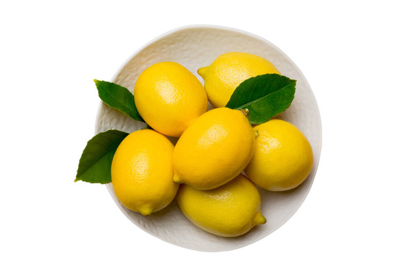 Fresh cutted lemon and whole lemons over round plate isolated on white background. Food and drink ingredients preparing. healthy eating theme top view with copy space. - Photo, Image