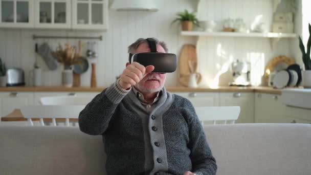 Emocionado hombre mayor maduro usando gafas de realidad virtual metaverse VR auriculares en casa. Abuelo tocando el aire durante la experiencia VR en casco de realidad virtual. Videojuego de simulación de alta tecnología - Imágenes, Vídeo