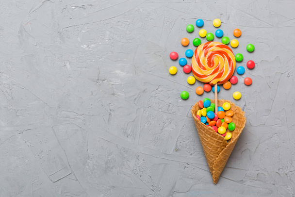 waffle cone full of assorted traditional candies falling out on colored background with copy space. Happy Holidays sale concept. - Фото, изображение