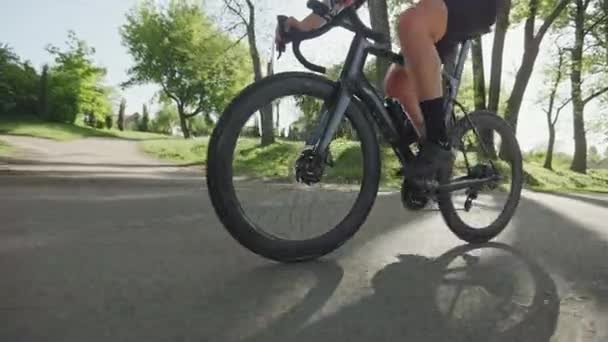 Cropped view of male cycler pedaling along paved driveway on racing bike using sunny day in city park. Efficient sports person in tight-fitting clothes conducting slow recreational trip outdoors. - Footage, Video
