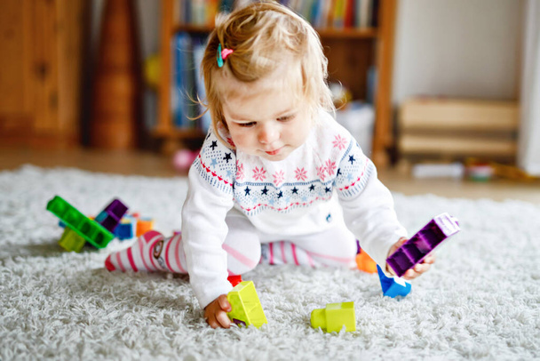 Adorable niña jugando con juguetes educativos en el vivero. Feliz niño sano divirtiéndose con coloridos bloques de plástico diferentes en el hogar. Aprendizaje lindo del bebé, creación y construcción - Foto, imagen