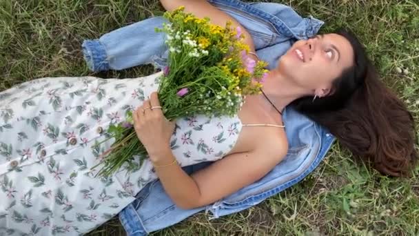 Dönüşümlü fotoğraf çekiminde, giyinmiş çok ırklı genç bir kadın canlı kır çiçekleriyle çayır çimlerinde uzanıyor. Tatlı kız hayal kuruyor, gülümsüyor, anılarda kayboluyor. Romantik anlar. Boşluğu kopyala - Video, Çekim
