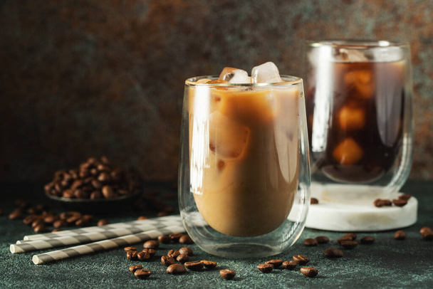 Jeges kávé egy magas pohárban tejszínhabbal, jégkocka és bab egy sötét betonasztalon. Hideg nyári ital csövek fekete háttér másolási hely. - Fotó, kép