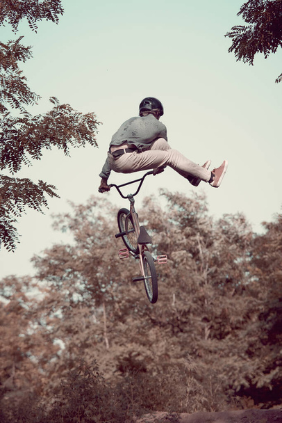 Back view dynamic image of young man in helmet riding bmx bike in forest, training, doing difficult and dangerous tricks. Concept of active lifestyle, sport, extreme, dynamics, hobby, freestyle - Zdjęcie, obraz