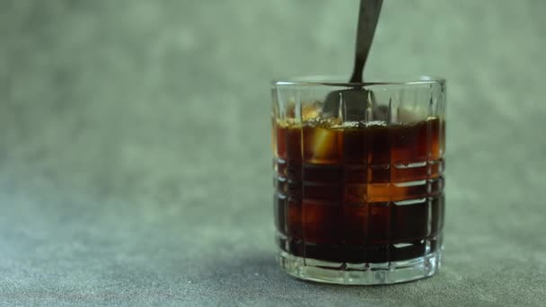 Handen roeren verfrissende ijskoffie in een glas met een lepel - Video
