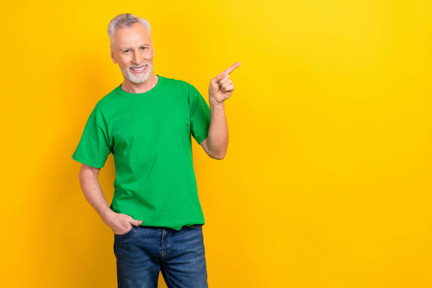 Photo of good mood charming guy dressed green t-shirt showing finger empty space isolated yellow color background. - Valokuva, kuva