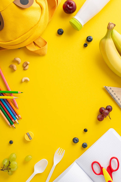 Instill wellness values at school - vertical top view fresh fruits, berries, nuts, yogurt, cutlery, stationery, color pencils, scissors, diary, funny backpack on yellow background with space for text - Photo, Image