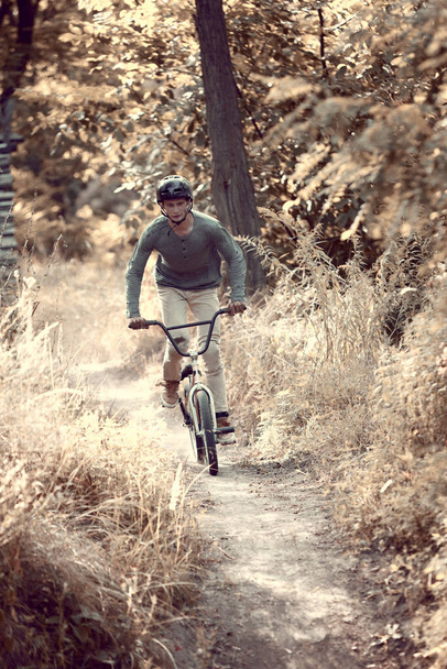 Developing speed during ride. Young man riding on bmx bike in forest, doing tricks, training. Concept of active lifestyle, sport, extreme, dynamics, hobby, freestyle - Photo, Image