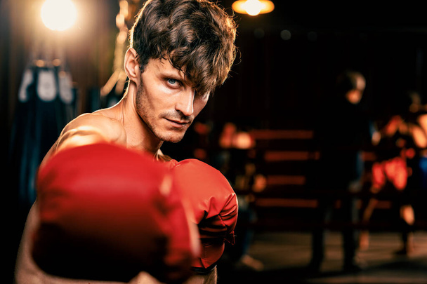 Boxkämpfer ohne Hemd posiert, kaukasischer Boxer schlägt seine Faust vor der Kamera in aggressiver Haltung und bereit, im Fitness-Studio zu kämpfen, im Hintergrund Trettasche und Boxausrüstung. Impulse - Foto, Bild