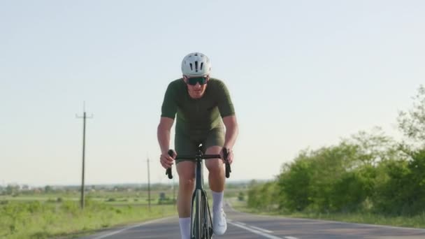 Widok z przodu sportowca w stroju sportowym Wheeling Road Bike w dynamicznym tempie między polami w słoneczny dzień. Keen kaukaski rowerzysta rozwija koncentrację i świadomość obecnej chwili na przejażdżce. - Materiał filmowy, wideo