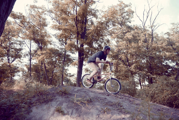 Young man in helmet training outdoors in forest, riding bmx bike, doing tricks. Autumn ride, extreme man. Concept of active lifestyle, sport, extreme, dynamics, hobby, freestyle - Photo, Image
