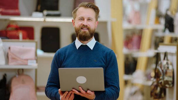 Small business concept good looking salesman smiling in front of the camera while holding his laptop. - 写真・画像