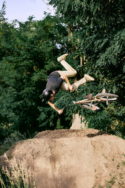Dangerous sport. Young man riding on hill in park, forest on bmx bike, doing tricks and falling down. Concept of active lifestyle, sport, extreme, dynamics, hobby, freestyle - Foto, afbeelding