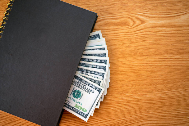 Koncept finančních úspor: zátiší stovek bankovek v osobním notebooku na pracovním stole s kopírovacím prostorem - Fotografie, Obrázek