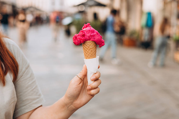 Színes, ízletes jégkrém tölcsér a kézben. Közelkép a nő kezét tartó friss gofri kúp rózsaszín fagylalt szabadban - Fotó, kép