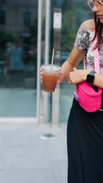 Egy vonzó, fiatal nő kávéval és okostelefonnal siet a csúcsforgalomban. Kiváló minőségű 4k felvételek - Felvétel, videó
