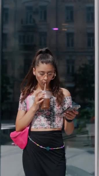 Elinde canlandırıcı bir içecek olan genç ve güzel bir kız akıllı telefonuyla mesajlaşıyor. Yüksek kalite 4k görüntü - Video, Çekim