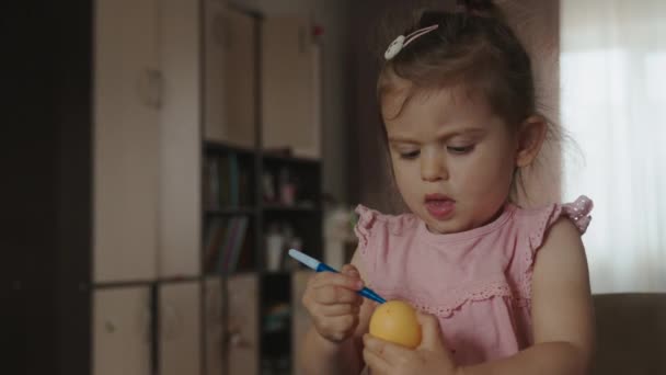 Ευτυχισμένο κορίτσι παιδί κρατώντας αυγό και σχέδιο σε αυτό με τσόχα στυλό άκρη, ενώ περνούν το χρόνο τους στην κουζίνα. Καλό Πάσχα.. - Πλάνα, βίντεο