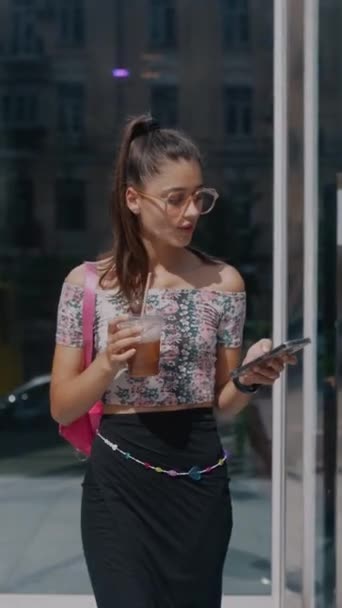 Uma jovem elegante e radiante nas ruas da cidade com uma bebida gelada e um smartphone nas mãos. Imagens 4k de alta qualidade - Filmagem, Vídeo