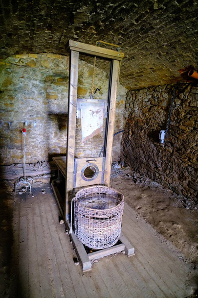 W ciemnej piwnicy jest mało światła. Gilotyna, średniowieczne narzędzie kary, stoi z koszykiem z wikliny. - Zdjęcie, obraz