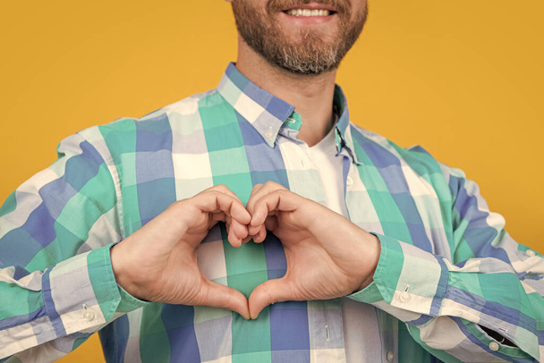 cropped bearded caucasian man in shirt show love heart isolated on yellow background. caucasian casual man with love heart in studio. photo of man showing love heart. man gesturing love heart. - Foto, Bild
