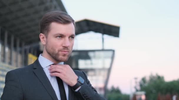 Kaukázusi fiatal üzletember igazítja a nyakkendőjét és félrenéz. Irodai dolgozó a szabadban. - Felvétel, videó