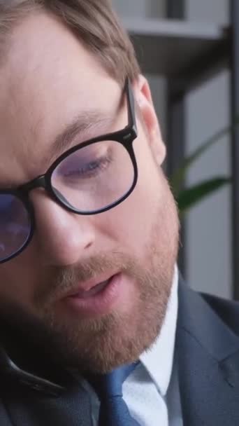 Close-up of a male bank employee talking on a mobile phone in the office. A young businessman is making a phone call at the workplace in slow motion. Vertical video - Séquence, vidéo
