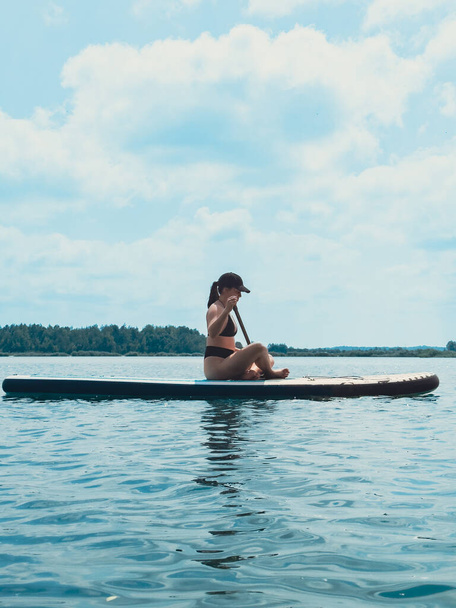 beautiful woman sitting down on the supboard paddling in the middle of the lake - Photo, Image