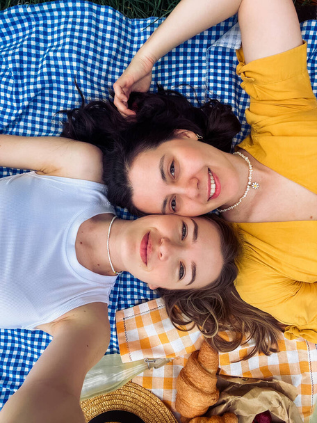 İki arkadaş açık hava pikniği için mavi bir battaniyeyle selfie çekiyorlar. - Fotoğraf, Görsel