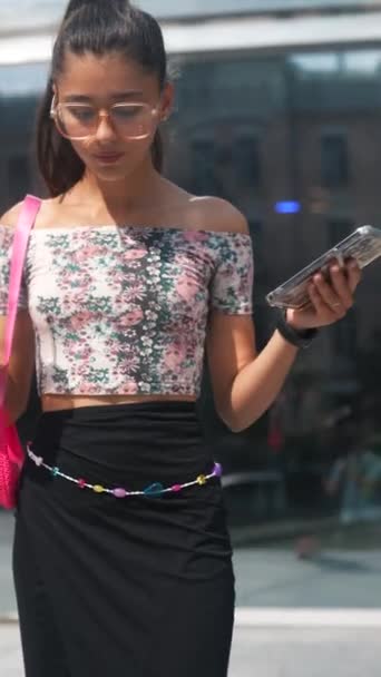 Uma jovem elegante e brilhante nas ruas da cidade com um café gelado e um smartphone nas mãos. Imagens 4k de alta qualidade - Filmagem, Vídeo