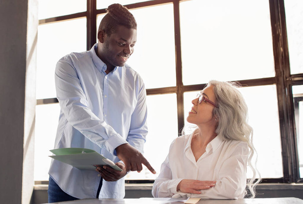 На робочому місці. афроамериканський бізнесмен надаючи керівництво та підтримку працівникам жінки коворкером починаючи свою нову роботу, вказуючи пальцем на столі в офісі - Фото, зображення