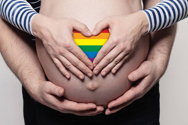 Gelukkig familieconcept. Man omarmt zwangere vrouw buik en hart met LGBT vlag - Foto, afbeelding